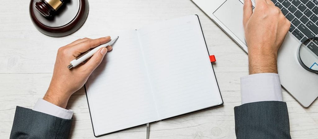 Advogado, anotando algo em seu caderno e seu notebook.