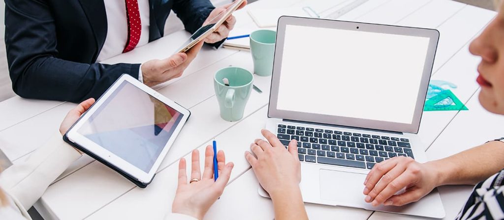 Conversa entre três pessoas, estão usando tablet e notebook.