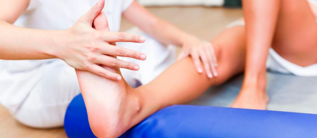 Mulher fazendo fisioterapia no pé de uma pessoa.
